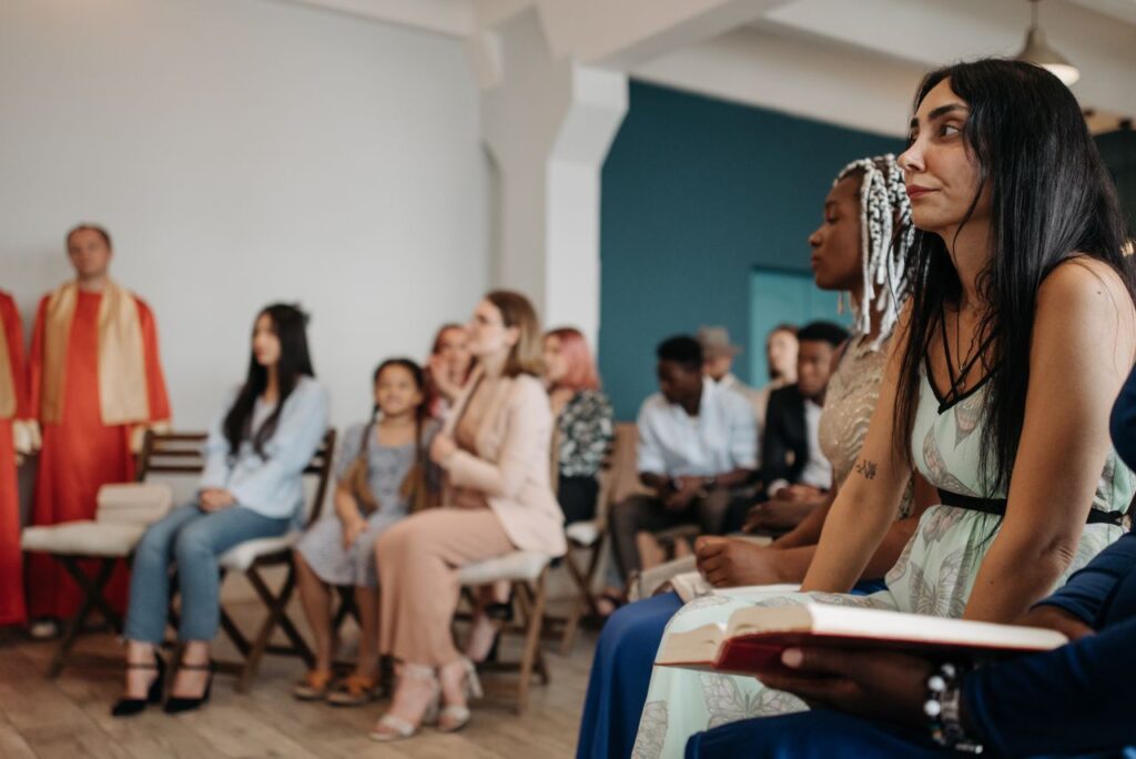 A multi-ethnic group of people attentively listening during a religious gathering indoors.